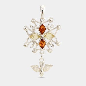 Peut inclure: Pendentif en argent avec un motif de flocon de neige, orné d'incrustations en forme de losange ambrées et jaunes. Un petit pendentif en forme de colombe est suspendu en dessous. Le pendentif est détaillé et poli.