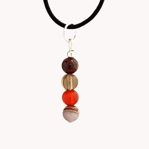 Peut inclure: Un collier avec un pendentif argenté composé de quatre perles rondes dans des tons de brun, orange et gris. Les perles sont enfilées sur un cordon noir.