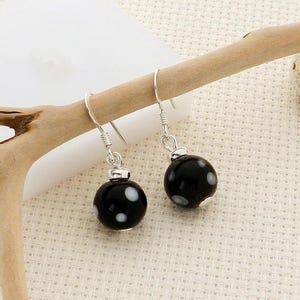 May include: A pair of black and white polka dot earrings. The earrings have a round, glossy black bead with white polka dots. The earrings are suspended from silver-colored hooks.