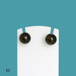 Peut inclure: Une paire de boucles d'oreilles clous noires avec un design rond légèrement texturé. Les boucles d'oreilles sont présentées sur une carte blanche.