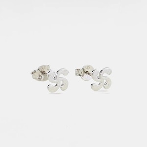 May include: A pair of sterling silver stud earrings featuring a four-armed curved cross design, known as a lauburu. Each earring has a post back and is stamped with 925 to indicate the silver content, showcasing a polished metallic finish.