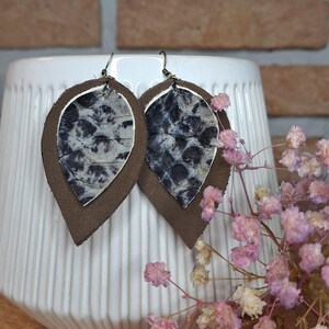 Può includere: Un paio di orecchini in pelle marrone con un design a motivi bianco e nero. Gli orecchini hanno la forma di lacrime e uno stile semplice ed elegante.