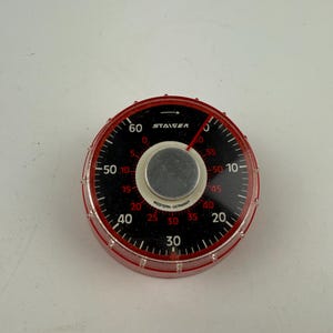 Könnte beinhalten: Ein schwarz-roter Timer mit einer durchsichtigen Plastikabdeckung. Der Timer hat ein weißes Zifferblatt mit schwarzen Zahlen und einem roten Pfeil. Der Timer ist mit "STAGER" und "WESTERN GERMANY" beschriftet.