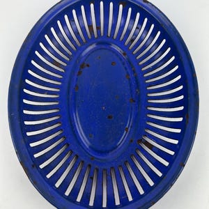Può includere: Un cesto di metallo blu ovale con un design decorativo tagliato. Il cesto ha una superficie liscia, leggermente usurata.