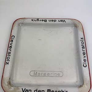 Könnte beinhalten: Ein rechteckiges weißes Tablett mit rotem Rand. Auf dem Tablett sind die Wörter "Cleverstolz" und "Van den Bergh's" in Schwarz aufgedruckt. Das Wort "Margarine" ist in der Mitte des Tabletts aufgedruckt.