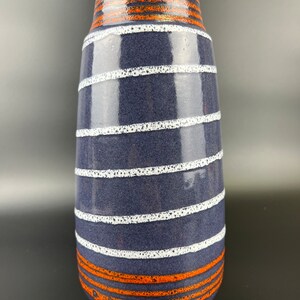 Könnte beinhalten: Eine blaue und weiße Keramikvase mit orangefarbenen Streifen. Die Vase hat eine strukturierte Oberfläche und eine abgerundete Form.