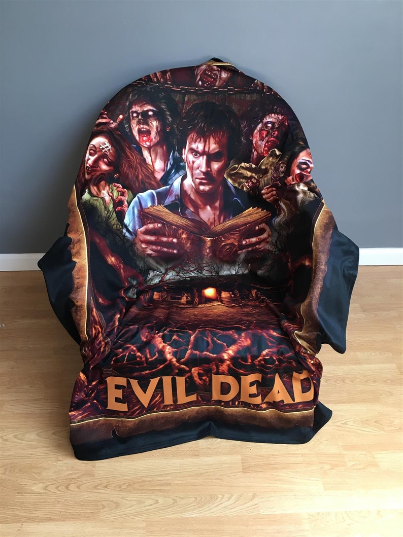 Pu&ograve; includere: Coperta in pile nera e arancione con una grafica di un uomo che legge un libro circondato da zombie. Il testo "Evil Dead" &egrave; stampato sul fondo della coperta.