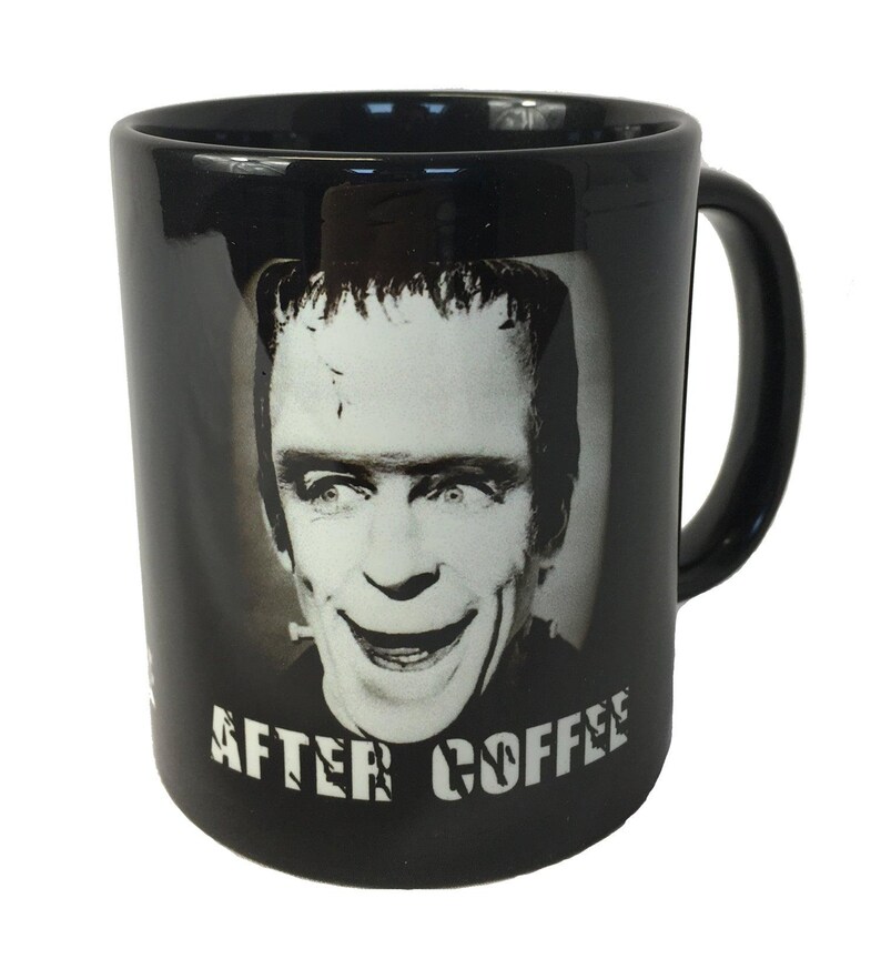Op de afbeelding: Zwarte koffiemok met een zwart-wit afbeelding van een lachend monster. De mok heeft de woorden "AFTER COFFEE" in witte blokletters. De mok heeft een zwart handvat.