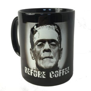 Op de afbeelding: Zwarte keramische koffiemok met een grijswaardenafbeelding van Frankenstein's monster. De mok heeft een zwart handvat en de woorden "BEFORE COFFEE" zijn in witte blokletters onder de afbeelding gedrukt. Een novelty item.