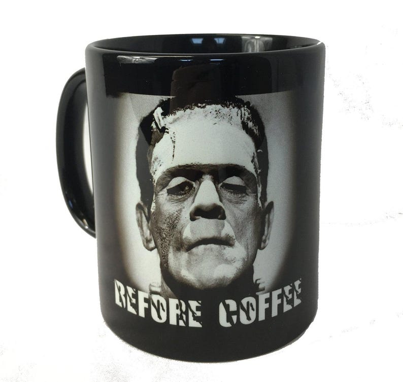 Op de afbeelding: Zwarte keramische koffiemok met een grijswaardenafbeelding van Frankenstein's monster. De mok heeft een zwart handvat en de woorden "BEFORE COFFEE" zijn in witte blokletters onder de afbeelding gedrukt. Een novelty item.