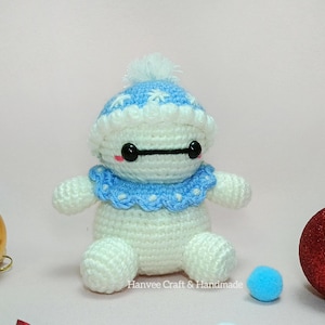 May include: A handmade crochet doll in white and blue, resembling a character with a round body, arms, and legs. It wears a blue hat and collar with white trim. The doll has black eyes and a black line for a mouth. The text "Hanvee Craft & Handmade" is at the bottom.