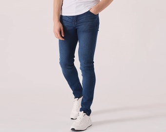 May include: A man wearing a white t-shirt and blue jeans. He is standing with his right hand in his pocket and looking to the left.