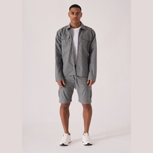 May include: A gray zip-up jacket and matching cargo shorts. The jacket has two flap pockets on the chest and the shorts have multiple pockets.