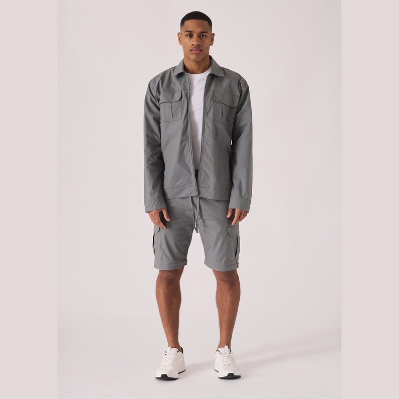 May include: A gray zip-up jacket and matching cargo shorts. The jacket has two flap pockets on the chest and the shorts have multiple pockets.