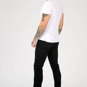 K&ouml;nnte beinhalten: Eine Person tr&auml;gt ein wei&szlig;es T-Shirt und eine schwarze Jeans. Die Person steht mit dem R&uuml;cken zur Kamera und schaut &uuml;ber die Schulter.