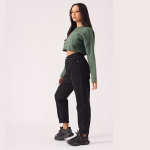 May include: A woman wearing a green cropped sweatshirt and black high-waisted jeans. She is wearing black sneakers.