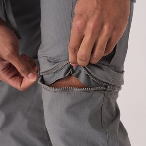May include: Gray pants with zippered legs that can be converted to shorts. The zipper is being pulled down to show the shorts underneath.