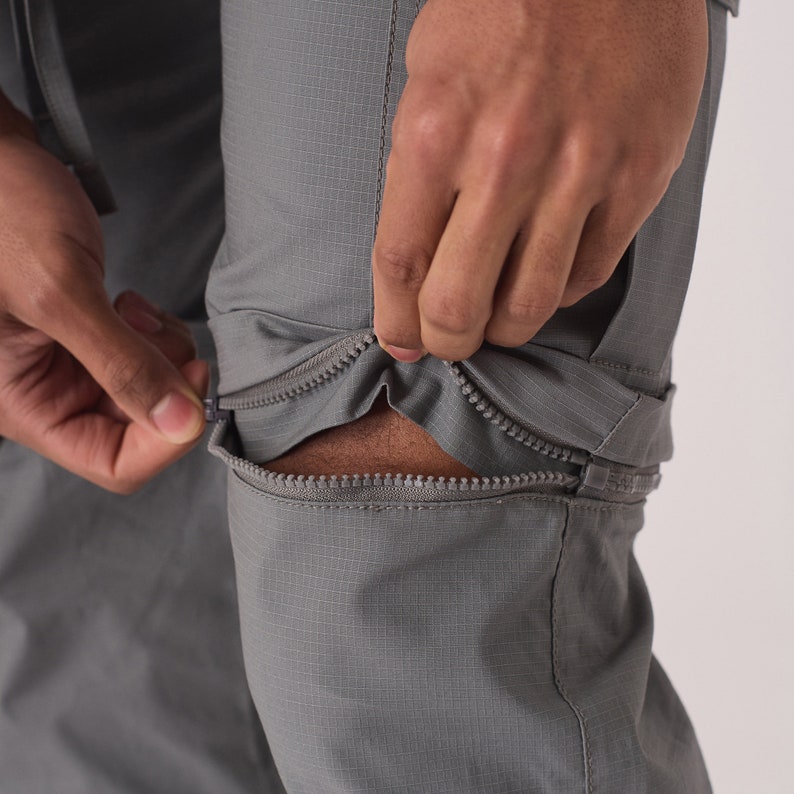 May include: Gray pants with zippered legs that can be converted to shorts. The zipper is being pulled down to show the shorts underneath.