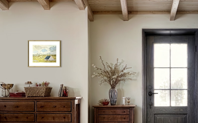 May include: A framed print of a watercolor painting depicting a small white house with a blue roof in a field. The house is surrounded by green grass and yellow flowers. The sky is blue with white clouds.