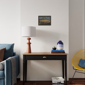 May include: A black console table with a wooden top and a single drawer. The table has a brass knob and is decorated with a framed landscape painting, a lamp, a vase with a succulent, and a stack of books.