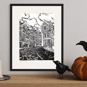 May include: A black and white line drawing of a city street with buildings on either side. The street is cobblestone and there is a building in the background with a sign that says "The Old Curiosity Shop".