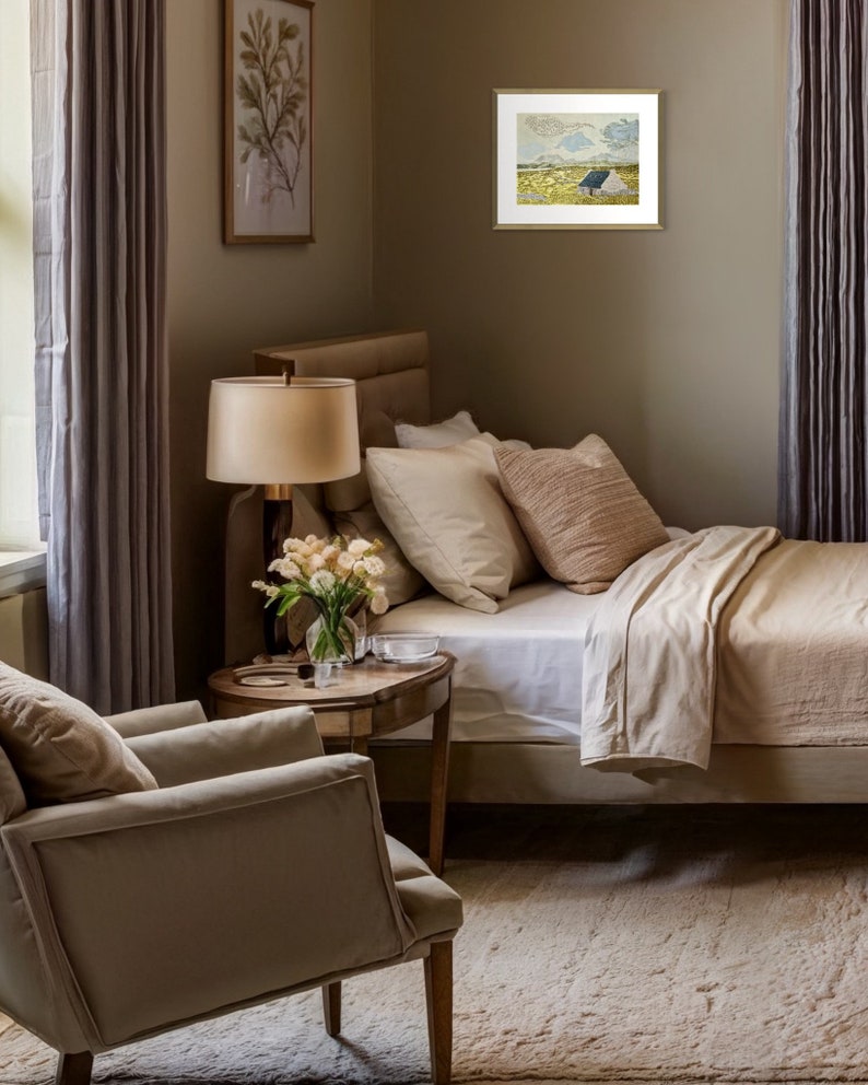 May include: A beige bedroom with a white bed, a beige armchair, a side table with a lamp, and a framed painting of a landscape with a small house on a hill.