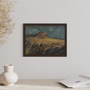 May include: A framed painting depicting a mountainous landscape with a cloudy sky. The mountain is brown and the sky is a pale blue with white clouds. The painting is in a dark brown frame.
