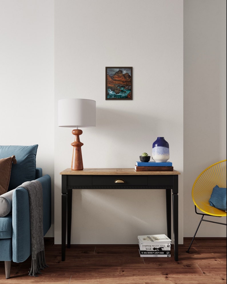 May include: A black console table with a wooden top and a single drawer. The table is decorated with a lamp, a vase, and a stack of books. A blue sofa and a yellow chair are visible in the background.