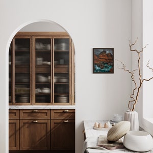 May include: A modern kitchen with wooden cabinets, a marble worktop, and a glass-fronted cabinet. A framed landscape painting hangs on the wall, and a vase with a dried branch sits on a marble worktop.