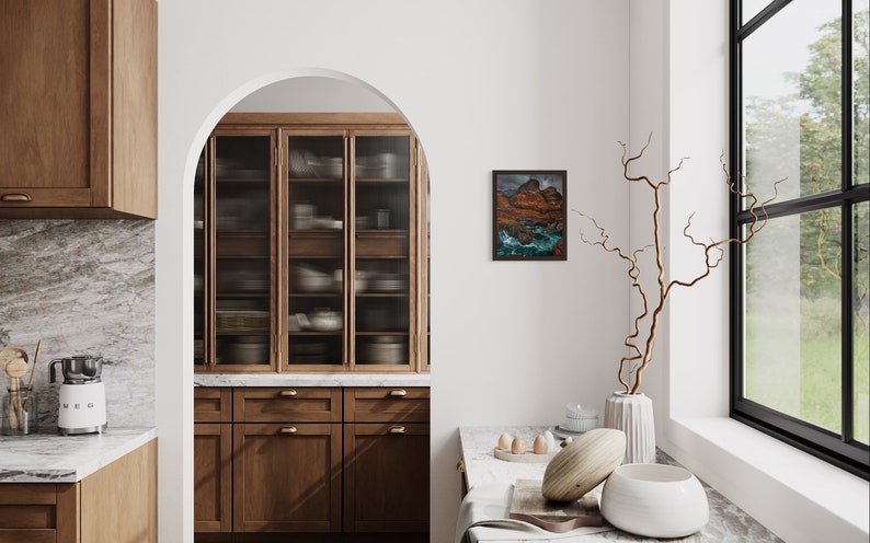 May include: A modern kitchen with wooden cabinets, a marble worktop, and a glass-fronted cabinet. A framed landscape painting hangs on the wall, and a vase with a dried branch sits on a marble worktop.