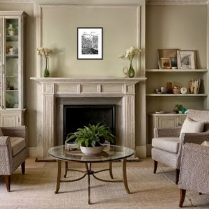 May include: A living room interior with two armchairs, a coffee table, a fireplace, and a glass-front cabinet. The walls are painted a light green color. The furniture is upholstered in a light gray fabric. The coffee table is made of glass and metal. The fireplace is made of white stone. The cabinet is made of wood and glass. A black and white framed print hangs above the fireplace.