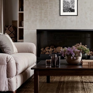 May include: A black and white illustration of a city street with buildings and cobblestone streets. The illustration is framed in a black frame and hanging on a wall above a fireplace.