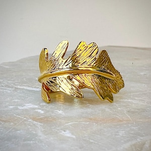 Puede incluir: Un anillo de oro en forma de hoja con una superficie texturizada.