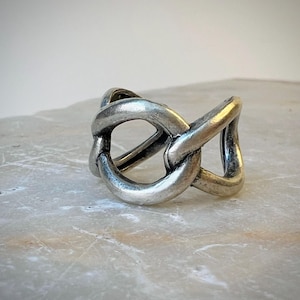 May include: A silver ring with a woven design. The ring is thick and has a wide band.