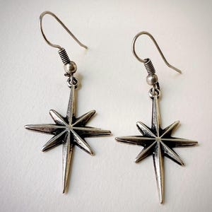 May include: A pair of silver star-shaped earrings with a simple, minimalist design. The earrings are suspended from a silver hook.