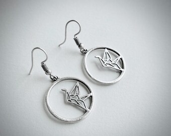 May include: A pair of silver earrings with a circular design featuring a cutout origami crane.