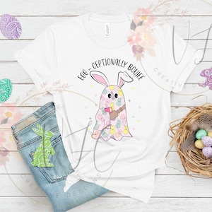 Puede incluir: Camiseta blanca con el texto "Egg-Ceptionally Boujee" y un diseño de conejo fantasma de dibujos animados. El conejo fantasma es rosa y está cubierto de patrones de Pascua. La camiseta se combina con vaqueros azules y decoraciones de Pascua.
