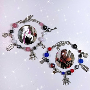 May include: Two beaded bracelets featuring Spider-Man comic book characters. Each bracelet has a silver chain with various charms, including a spider, stars, and a key. The bracelets incorporate black, red, pink, and blue beads.