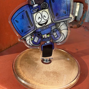 May include: A clear acrylic robot character with a smiling face, blue body, and white accents. The robot is mounted on a round, clear base. The robot's design includes a small screen and the text "ROB-O".