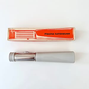 May include: A silver flashlight with a grey handle and a red and white box that says "Fléche lumineuse".