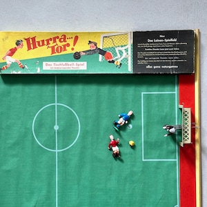 May include: Vintage tabletop soccer game with a green field, white lines, and miniature players. The box features illustrations of soccer players and the text "Hurra... Tor!" and "Das Tischfußball-Spiel".