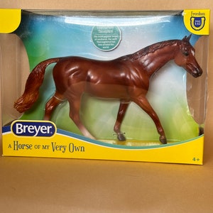 May include: A brown plastic Breyer horse model in a box. The box has a yellow background with the text "A Horse of My Very Own" and "Freedom Scale 1:12".