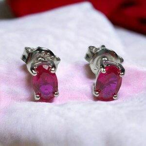 May include: A pair of silver stud earrings with oval-shaped pink gemstones. The earrings have a 925 stamp on the back.