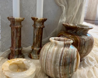 May include: Set of four decorative onyx vases in shades of brown, beige, and white. The vases are in different sizes and shapes, including a round bowl, a tall cylindrical vase, and two smaller cylindrical vases. The vases are arranged on a white fabric background.