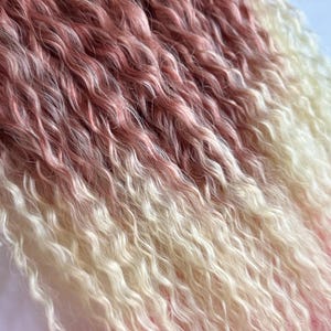 May include: Close-up of wavy hair extensions in shades of pink, white, and peach. The hair has a crimped texture and is arranged in a layered pattern. The extensions are likely for wigs or hair styling.