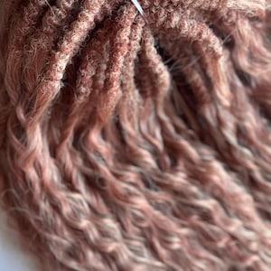 Peut inclure: Gros plan sur une mèche d'extensions de cheveux bouclés roses et blondes, attachée avec un ruban blanc. L'image montre la texture des cheveux, avec des boucles serrées et des mèches ondulées.