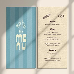 May include: A menu with a light blue striped cover and a beige interior. The cover has the words "The MENU" in a bold, off-white font, with illustrations of a bottle, shrimp, and a bottle. The interior lists starters, mains, and desserts.