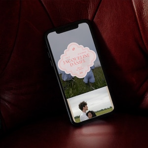 Peut inclure: Un smartphone affichant une invitation de mariage avec un motif floral rose et blanc. L'invitation indique "Jacqueline & Daniel" avec la date "15 juillet 2023". Le téléphone est sur une surface en cuir rouge.