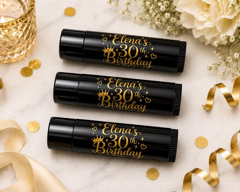 May include: Three black lip balm tubes with gold text that reads "Elena's 30th Birthday" with a crown and hearts. The tubes are arranged on a marble surface with gold confetti, a candle, and ribbon.