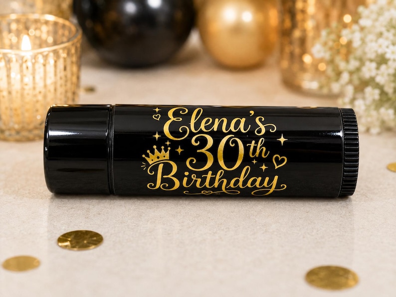 May include: A black cylindrical container with gold text that reads "Elena's 30th Birthday". The text is embellished with stars, a crown, and hearts. The background includes gold confetti and decorative items.